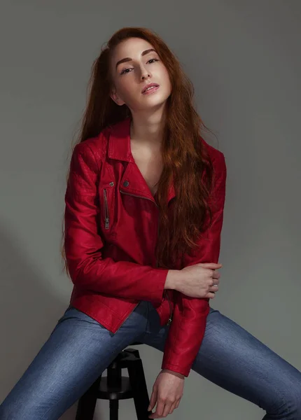 スタジオ ポートレート赤い革のジャケット 椅子温かみのある色調の上に座ってオープン肩に赤は長い髪を持つ女性のファッションとスタイルのコンセプト — ストック写真
