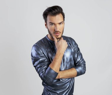 Yakışıklı genç adam dokunmadan parmağını ile dudakları ve kameraya benziyor. İnsan duyguları adam gümüş gri arka plan kopya alanı üzerinde raglan