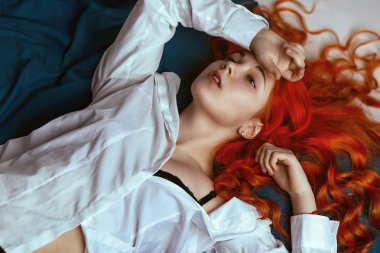 Muhteşem genç redhead kız çok uzun saçlı mavi sayfası yatakta uzanarak Beyaz gömlekli. Yan bakış yukarıda