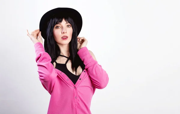 Retrato de moda de chica morena elegante sonriente con labios rojos en sombrero negro de moda y suéter rosa posando sobre la pared gris. Humor positivo . —  Fotos de Stock