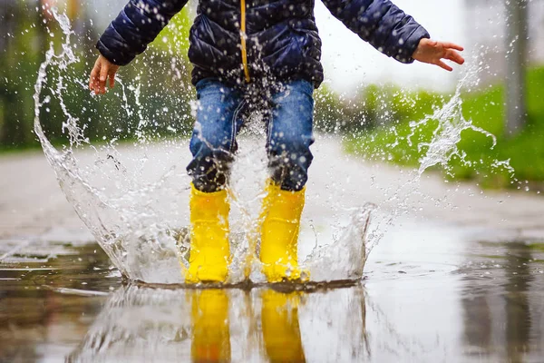 Pernas de criança com botas de borracha amarelas pulam na poça em um passeio de outono — Fotografia de Stock