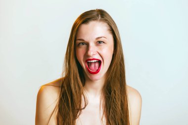 Sarı saçlı hayran kadın model, gri arka planda dağınık gözleri ve yaygın olarak açılan ağız ile bakıyor