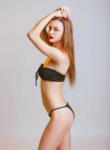 Vacker sportig flicka i svart Bikini poserar i studion. Foto av attraktiv blond tjej med Slim sport tonas kropp. Skönhet och kroppsvård koncept, varm ton färg — Stockfoto