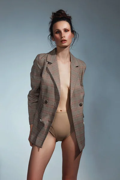 彼女の裸の体の上にジャケットを着てかわいいブルネットの女性とスタジオのファッションと美しさのコンセプトでポーズハイウエストの下着 — ストック写真