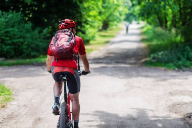 Kırmızı sırt çantalı, eski yol boyunca bisikletli genç bir adam.