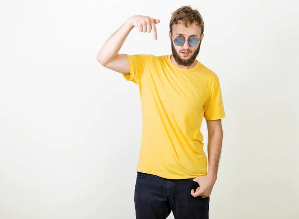 Homem barbudo em uma camiseta amarela e óculos redondos mostrando direção e aponta para baixo dedo, anuncia novo material para o chão, Pessoas, estilo de vida, conceito de promoção — Fotografia de Stock