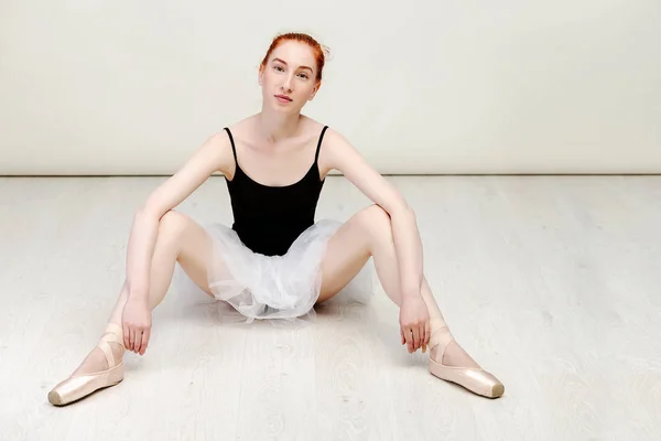 Mooie roodharige ballerina zit op de witte houten vloer ze draagt een lichte dans slijtage en een perzik Tutu. Ruimte kopiëren — Stockfoto