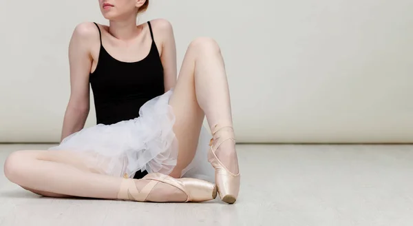 Pěkná baletka sedí na bílé dřevěné podlaze nosí lehké taneční oblečení a broskvovou Tutu. Kopírovat místo — Stock fotografie