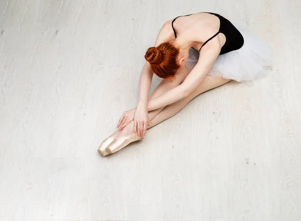 Bailarina ruiva agradável sentar-se em "morrendo cisne" posar no chão de madeira branca Ela usa um desgaste dança leve e um tutu pêssego. Foto vista superior. Horizontal. Espaço de cópia — Fotografia de Stock