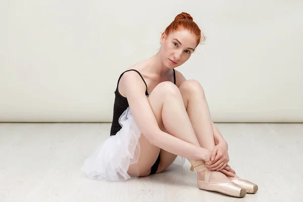 Mooie roodharige ballerina zit op de witte houten vloer ze draagt een lichte dans slijtage en een perzik Tutu. Ruimte kopiëren — Stockfoto