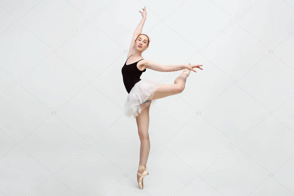 Young and incredibly beautiful ballerina is posing and dancing in a light grey studio full of light. The photo greatly reflects the incomparable beauty of a classical ballet art. Copy space