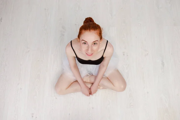 Portret mooie roodharige ballerina zit op de witte houten vloer ze draagt een lichte dans slijtage en een perzik Tutu. Top View foto. Horizontale. Ruimte kopiëren — Stockfoto