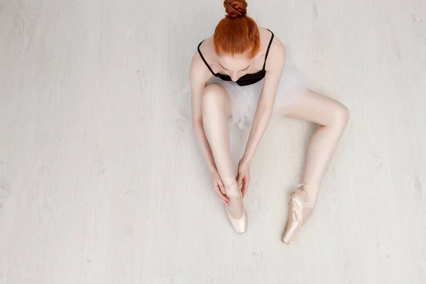 Nice ballerina zit op de witte vloer en jurken een beige Pointe schoen in de Studio. Ze draagt een lichte dans slijtage en een perzik Tutu. Top View foto. Horizontale. Ruimte kopiëren — Stockfoto