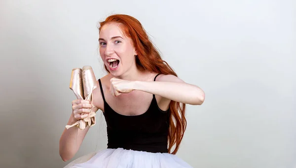 Retrato bailarina enojada sobre fondo gris. Emociones y sentimientos chica grita a sus zapatos sosteniéndolo en una mano y tratando de golpearlo con la otra mano — Foto de Stock