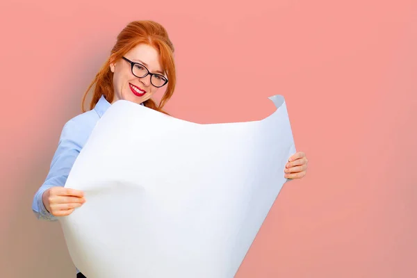 Kaukasiska Redhead flicka håller en tom duk i händerna och leende, rosa vägg på bakgrunden. Kopiera utrymme. Vacker ung affärskvinna med utkast affisch. — Stockfoto