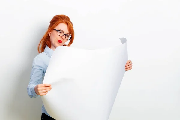 Kaukasiska Redhead flicka håller en tom duk i händerna och Grimace, grå vägg på bakgrunden. Kopiera utrymme. Vacker ung affärskvinna med utkast affisch. — Stockfoto