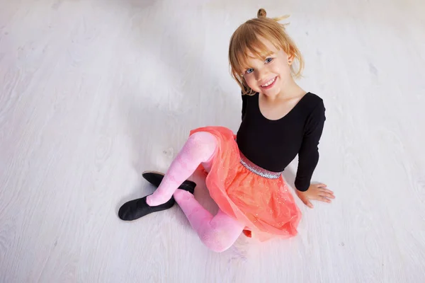 ピンクのチュチュの小さなダンサーの女の子。未就学児は堅木の床に座っています。白いスタジオでクラシックバレエを踊るかわいい子供。子供は踊るクラスの若いダンサー。テキストのスペースをコピー — ストック写真