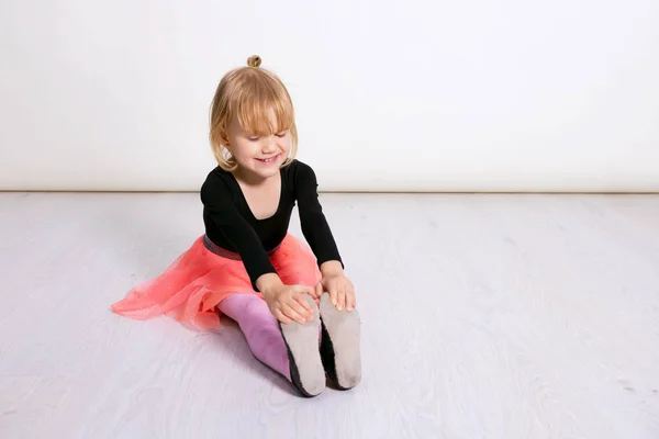 Pembe etekli küçük dansçı kız. Anaokulu çocuğu ahşap zeminde oturuyor. Beyaz stüdyoda klasik bale yapan şirin bir çocuk. Çocuklar dans eder. Sınıfta genç bir dansçı. Metnin için boşluk kopyala — Stok fotoğraf