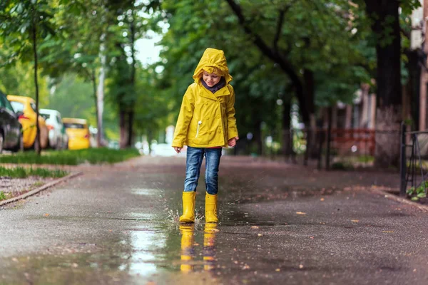 Do not be sad. child girl in yellow raincoat and rubber boots in puddle on a parking, autumn walk. Childhood happiness concept