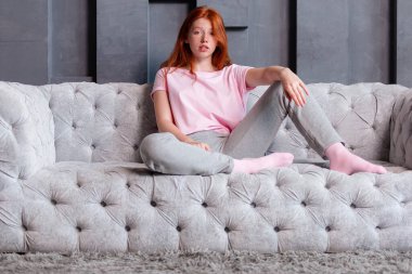 Evdeki kanepede oturan ve kameraya bakan güzel kızıl saçlı kadın.