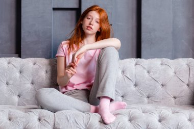 Evdeki kanepede oturan ve kameraya bakan güzel kızıl saçlı kadın.