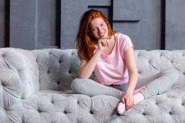 Evdeki kanepede oturan ve kameraya bakan güzel kızıl saçlı kadın.