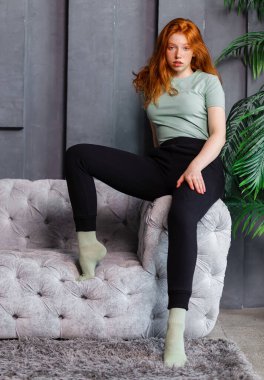 Odadaki kanepede gündelik kıyafetlerle oturan güzel seksi bir kızın portresi. Güzellik, kozmetik. Ev çekimi.