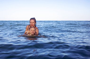 Anne küçük kızını kucağında tutuyor. Denizde yıkanırlar, bir sürü damla damlatırlar ve harika kahkahalar atarlar sıcak yaz günlerinde birlikte eğlenirler.