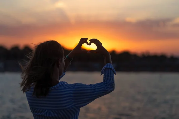 Woman making heart of hands at sea sunset