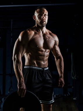 Ağırlıklı kaslı adam eğitimi. Koyu renk spor salonunda kaslarını çalıştıran acımasız, güçlü atletik adamlar..