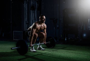 Ağırlıklarla antrenman yapan kaslı adam. Güçlü atletik adam egzersiz yapar. Vücut geliştirme uzmanı spor salonunun spot ışıkları altında egzersiz yapıyor..