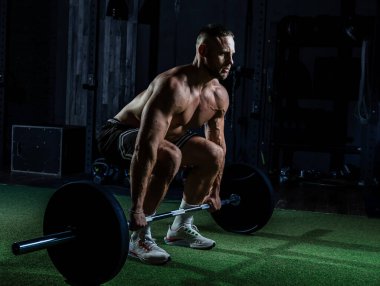 Ağırlıklı kaslı adam eğitimi. Koyu renk spor salonunda kaslarını çalıştıran acımasız, güçlü atletik adamlar..