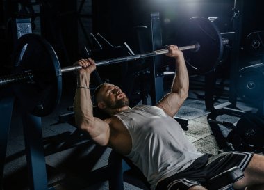 Ağırlıklı kaslı adam eğitimi. Koyu renk spor salonunda kaslarını çalıştıran acımasız, güçlü atletik adamlar..