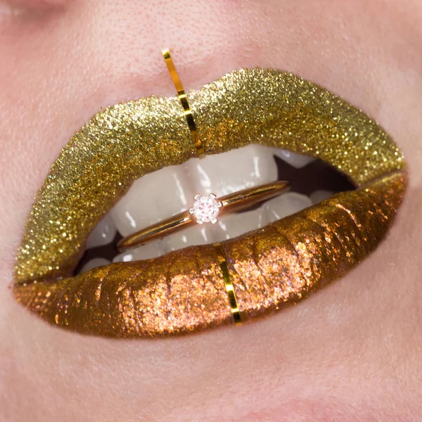 Vacker närbild med kvinnliga fylliga läppar med guldfärgad makeup. Glitter kosmetiska. Gyllene ring med lysande i munnen — Stockfoto