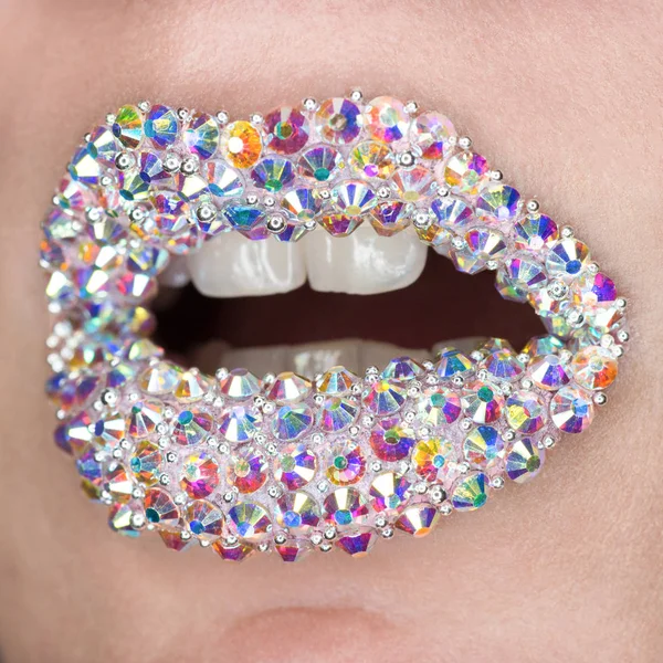 Belo close-up com lábios femininos com pedras preciosas coloridas brancas. Boca aberta com dentes brancos. Maquilhagem, arte labial — Fotografia de Stock