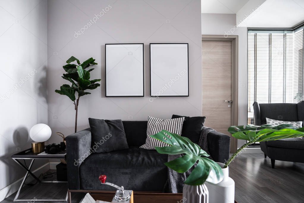 Cozy grey velvet sofa with soft pillows and blank frames on wall 