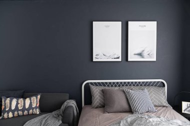 yatakta yastık ve duvarda çerçeveler ile gri renklerde rahat yatak odası iç