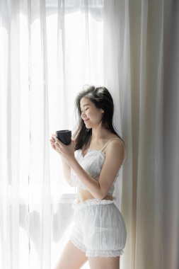 Asian women while reading book near window with shear curtain / 