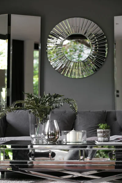 Cozy living room corner at home decorated with luxury rounded mirror and foldable mirror partition with artificial plant in glass vase and book on mirror coffee table in green home garden in reflection / cozy interior design / vintage style