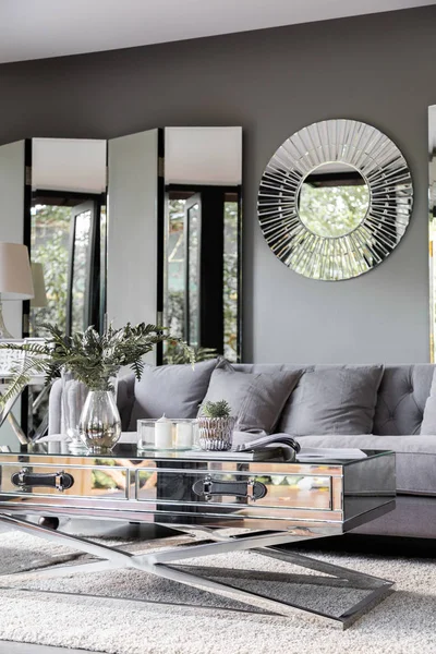 Cozy living room corner at home decorated with luxury rounded mirror and foldable mirror partition with artificial plant in glass vase and book on mirror coffee table in green home garden in reflection / cozy interior design / vintage style