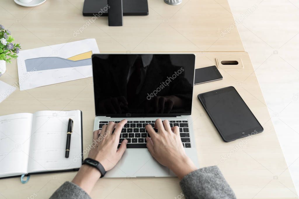 The businessman while typing information on a laptop with office accessories setting on wood table. /Business and technology concept/copy space