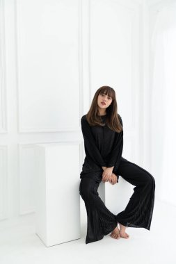 Asyalı kadınlar beyaz arka planda siyah dantel kumaş kostümlü beyaz taburede otururlar / kontrast konsepti / moda konsepti / kopyalama alanı