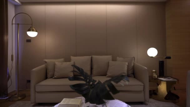 ベージュの革のソファとスタイリッシュな高級リビングルームの映像 金のステンレス製の壁ランプと背景の壁カバー 高級インテリア コピースペース — ストック動画
