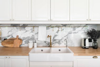 Mutfak aletleri ve beyaz seramik lavabo ile modern klasik mutfak içi ahşap tepesinde altın ayna musluğu ve arka planda mermer duvar / mutfak iç mimarisi