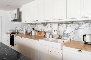 Mutfak aletleri ve beyaz seramik lavabo ile modern klasik mutfak içi ahşap tepesinde altın ayna musluğu ve arka planda mermer duvar / mutfak iç mimarisi