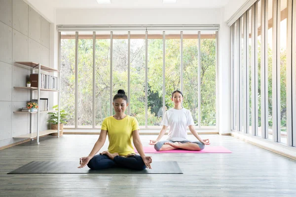 Two happy asian women in yoga poses in yoga studio with natural light setting scene / exercise concept / yoga practice / copy space / yoga studio