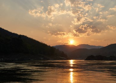 Laos 'taki Mekong nehrinde gün batımında. Luang Prabang bölgesinde Mekong nehrinde feribotla tur. Arka planda muhteşem kayalıklar ve plajlar var. Macera dolu orman atmosferi.