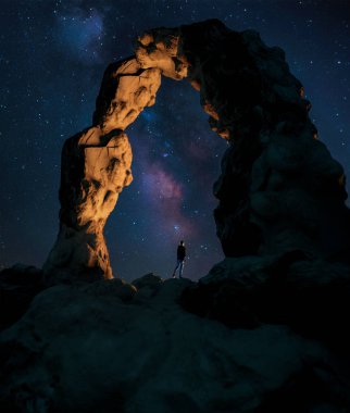 Kayalık kemerin altında duran ve yıldızlı gökyüzüne bakan adam 