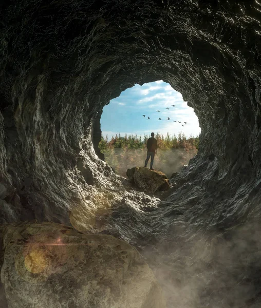 Man standing in cave and looking on wilde forest under blue sky