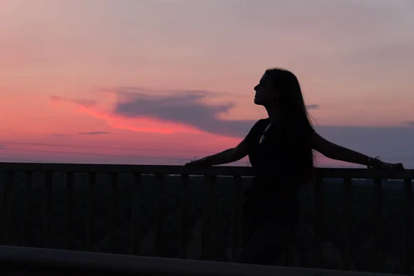 Bela jovem morena posando uma estrada no meio do campo ao pôr do sol, silhueta — Fotografia de Stock